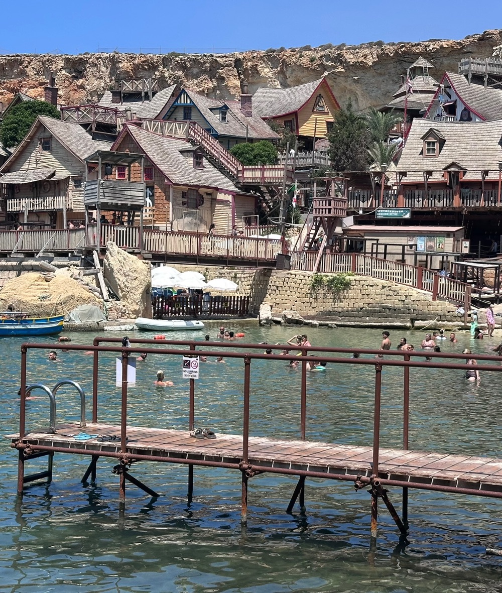 The wooden houses of Popeye Village on the bay, seen from a rusty pier over the water
